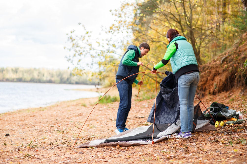 two people setting up a tent on the ground near a river