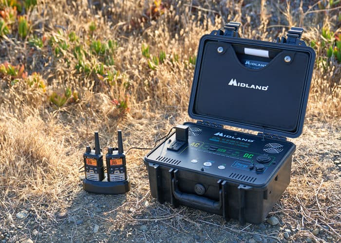 two walkie talkies next to a midland portable power station in a field of dry grass