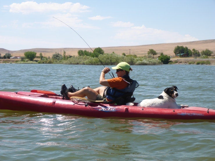 man on camping trip kayaks and fishes with dog on his boat