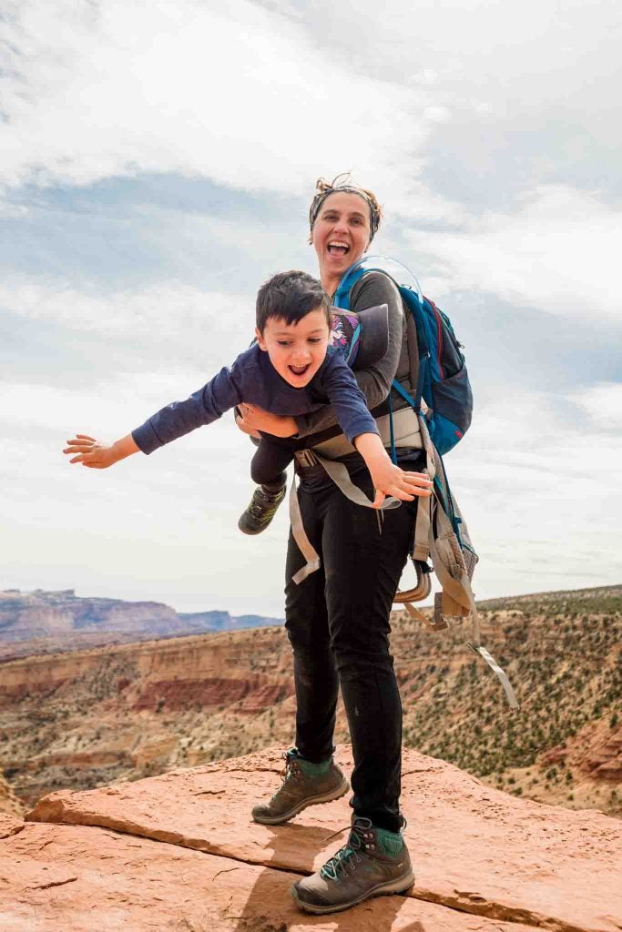 smiling mom holding son in airplane pose over canyon, via hike it baby