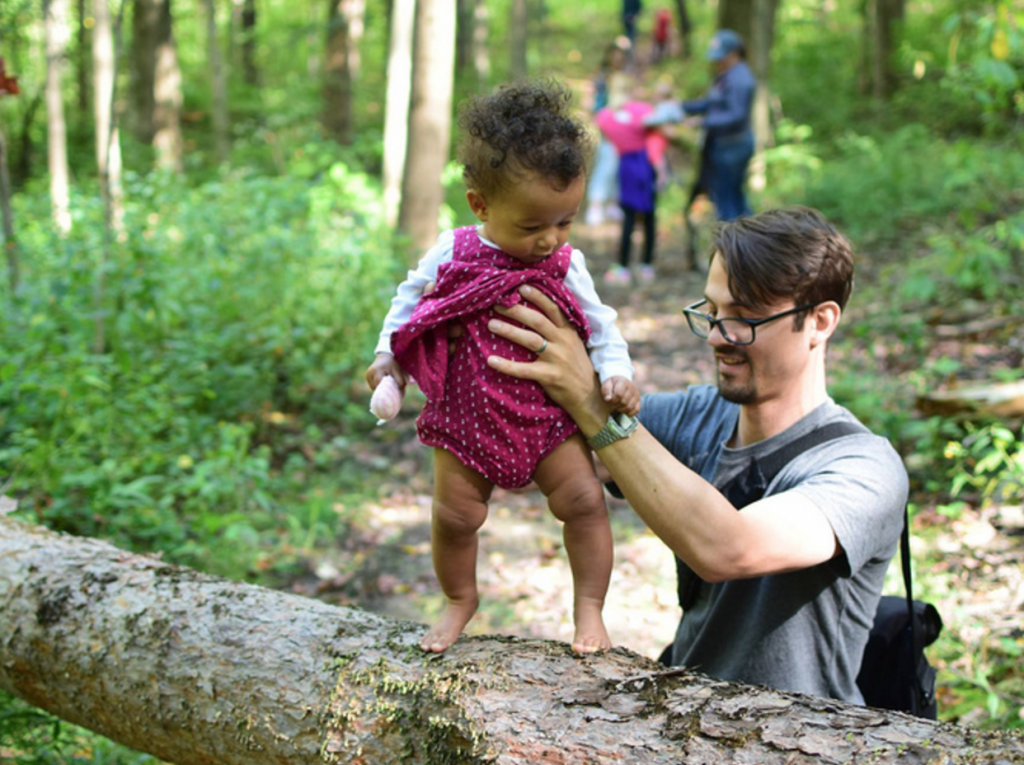 dad balances baby on log in forest, via hike it baby