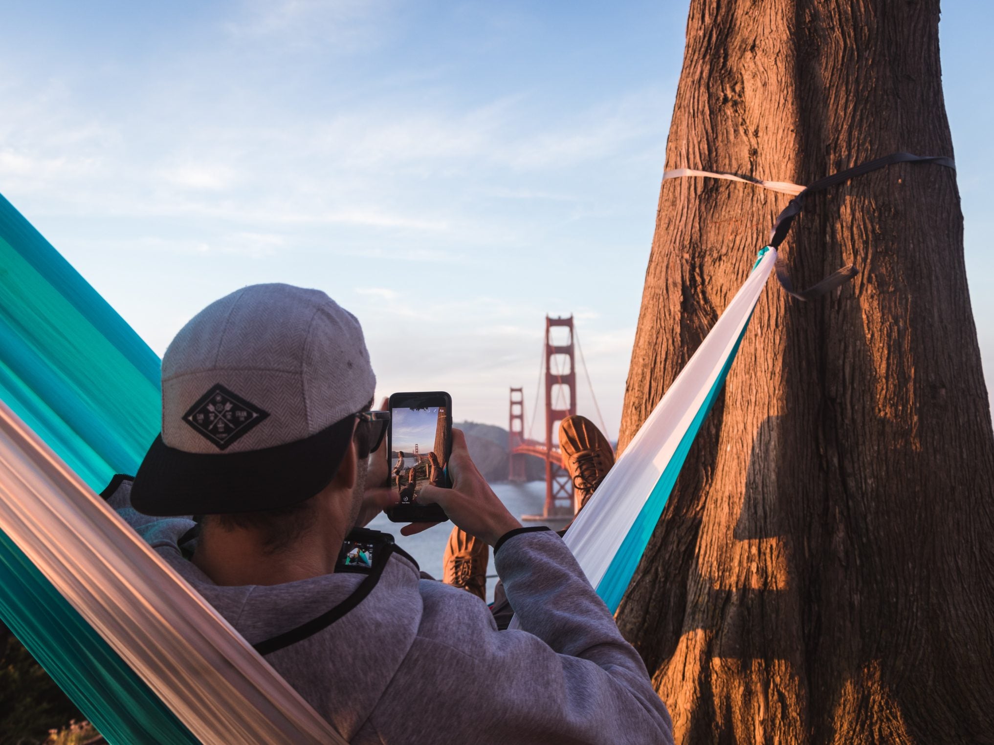 man lounges in hammock while photographing golden gate bridge in background