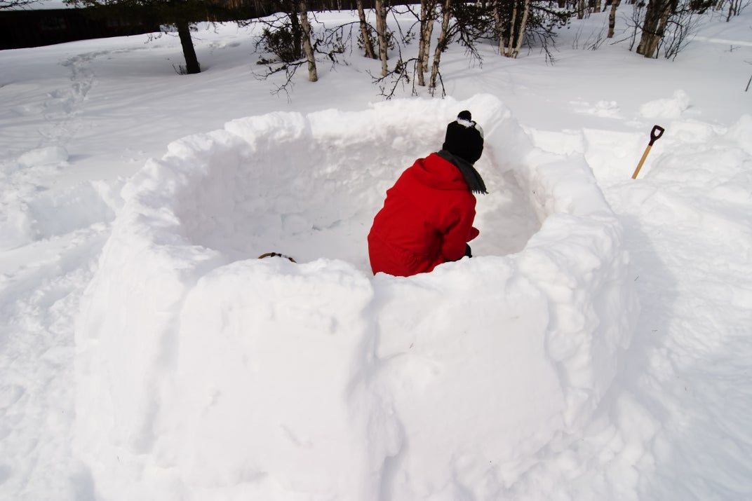 person in a red coat building the walls of an igloo in winter