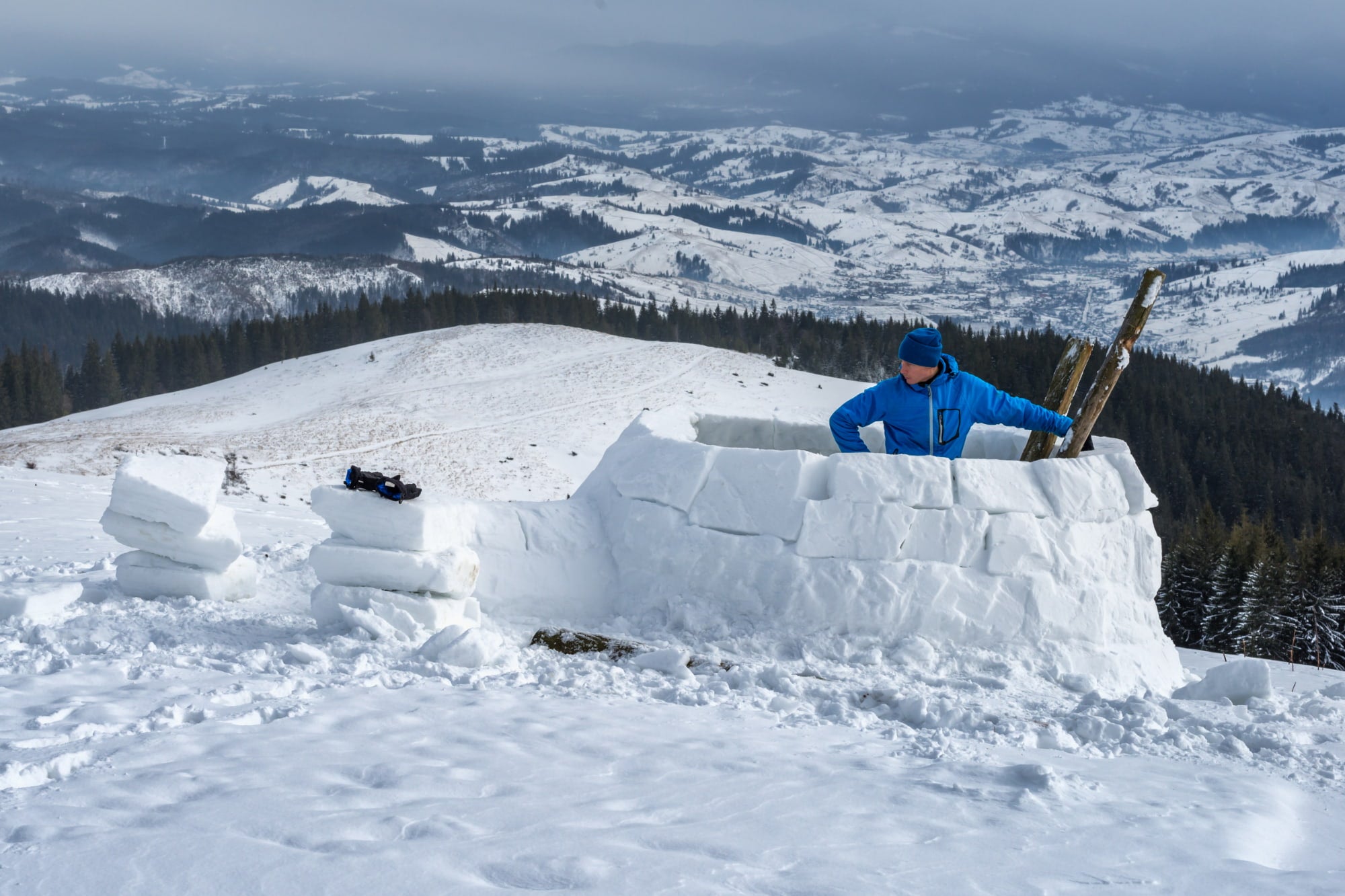 a man inside a half-built igloo on a snowy hill in the mountains