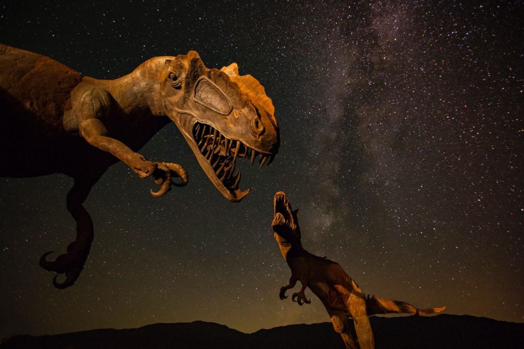 Esculturas de dinosaurios por la noche con las estrellas de fondo