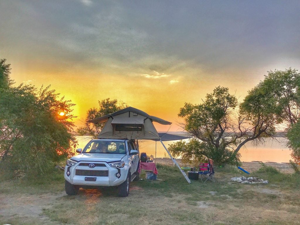 a car camper with a roof set up in front of a lake at dusk