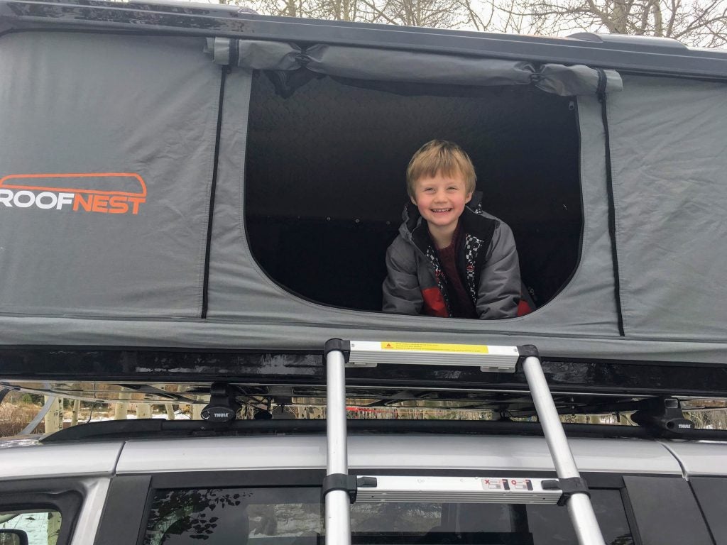 five year old boy poses in opening of roofnest roof top tent