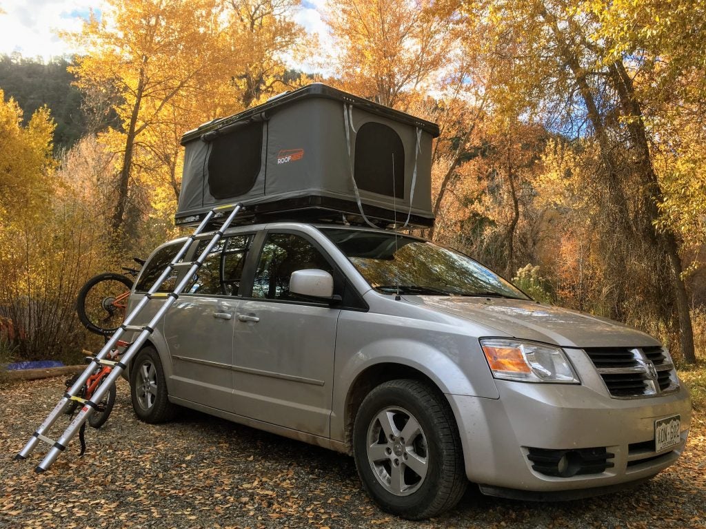 yellow fall foliage surrounds roofnest hard shell roof top tent installed on a grey minivan