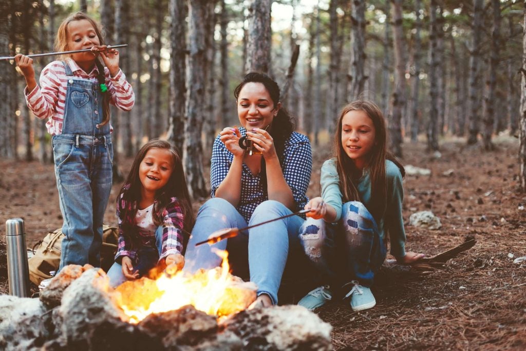 mom and three daughters roast marshmallows over the fire