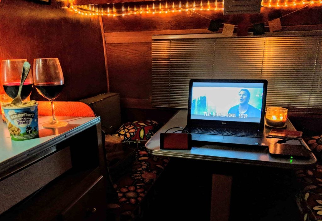 Wine glasses and ice cream pint beside a laptop playing a movie.