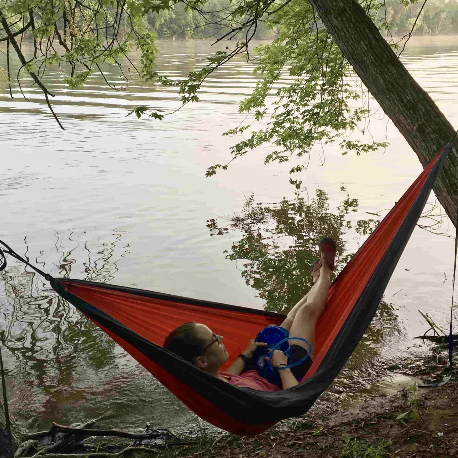 camper lounges in red hammock on riverfront