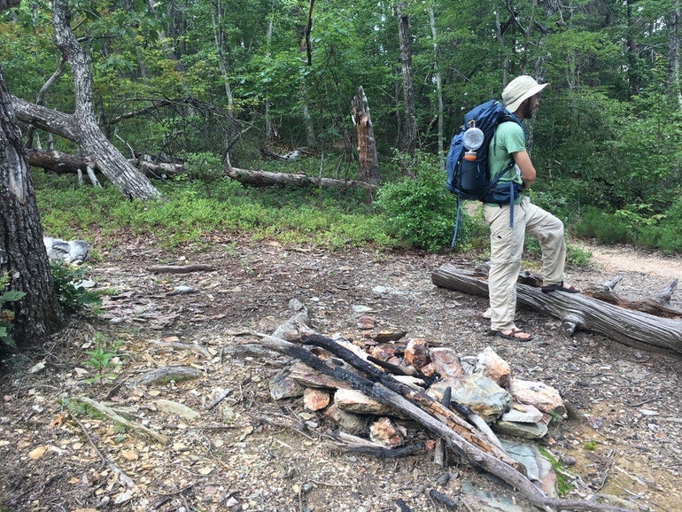 pinhoti trail hiker with bucket hat and blue backpack rests on a log near cave creek