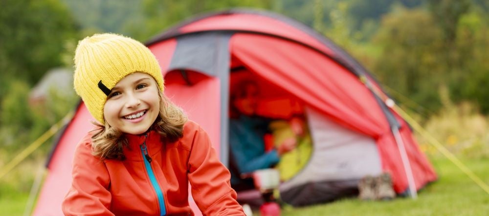 Smiling girl sits in campground with her kids camping gear
