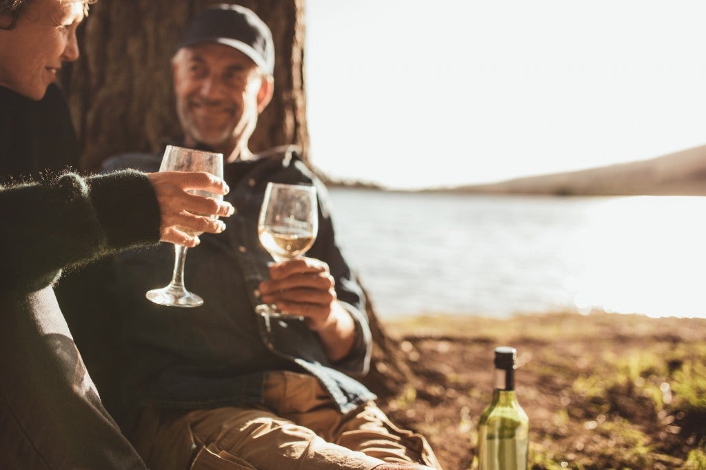 couple clinking two wine glasses together at their waterfront campsite