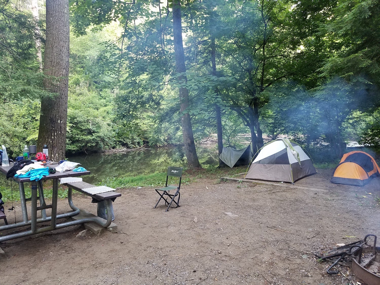 wooded, riverside campsite with multiple tents and a full picnic table at a...