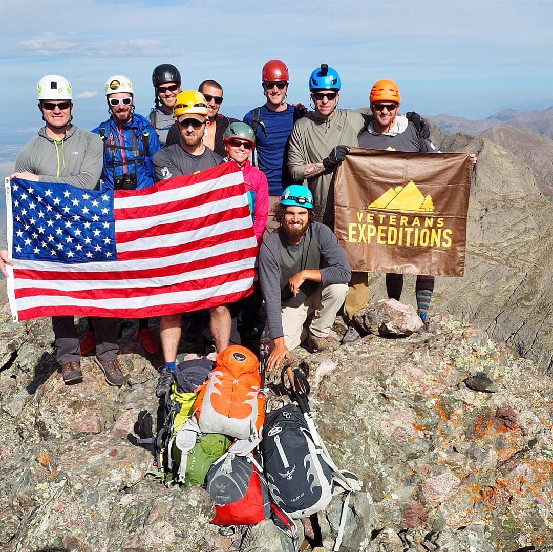 group of veterans on a rocky mountain summit with american flag and veteran expeditions f;ag