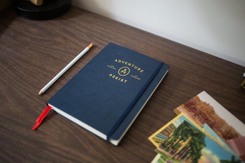 navy adventure assist camping journal on a wood desk 