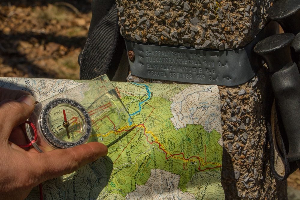 close up view of a hiker holding a compass over their map beside Appalachian trail marker