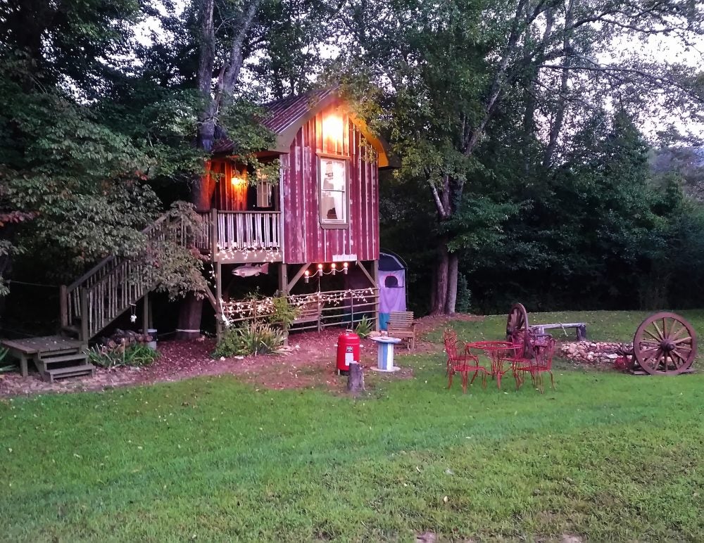 weathered red treehouse illuminated over a furnished lawn