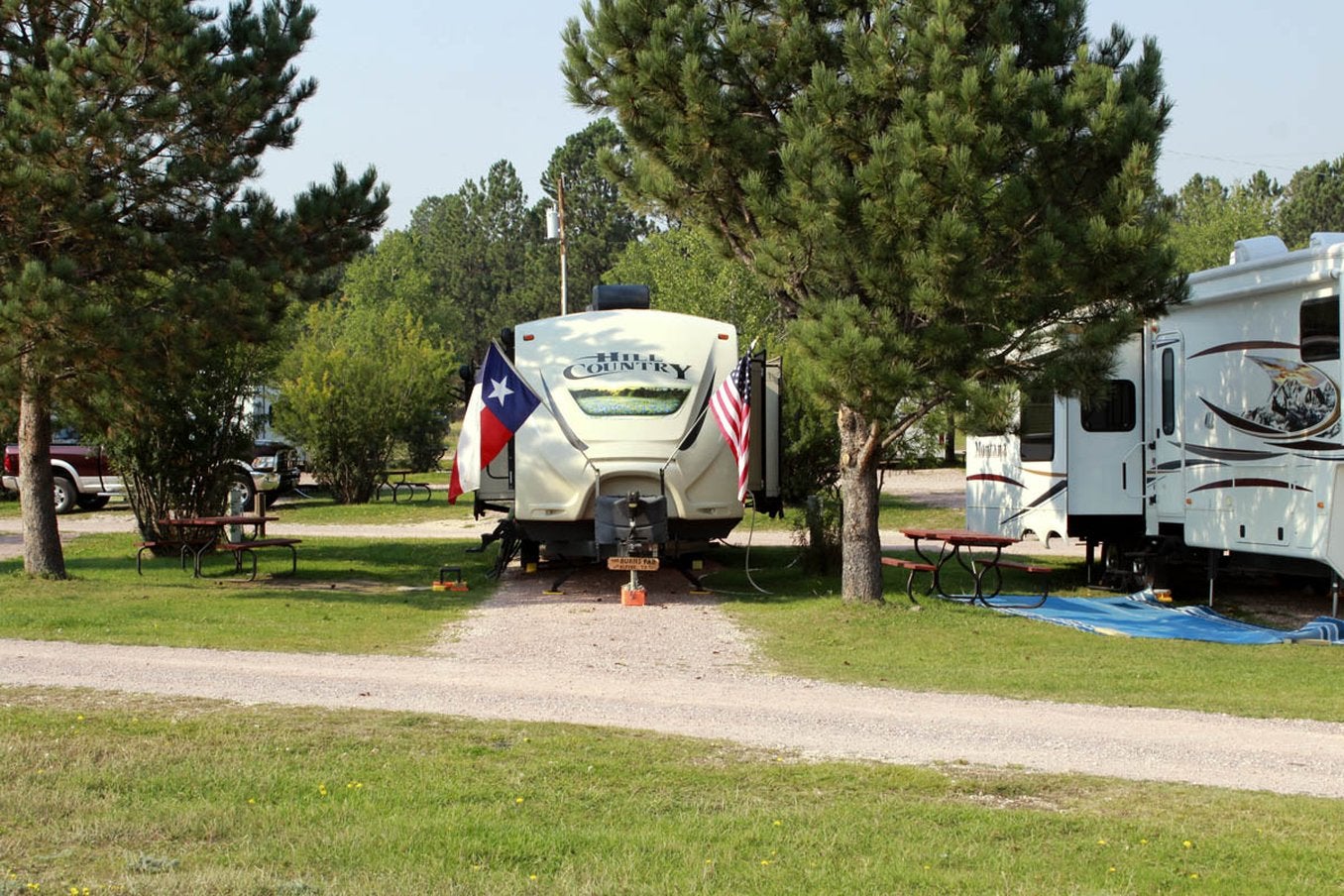 camper trailer backed into campsite between pine trees with a texas and american flag on each side