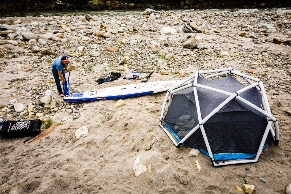 surfer prepares his board beside a heimplanet inflatable tent on a rocky beach