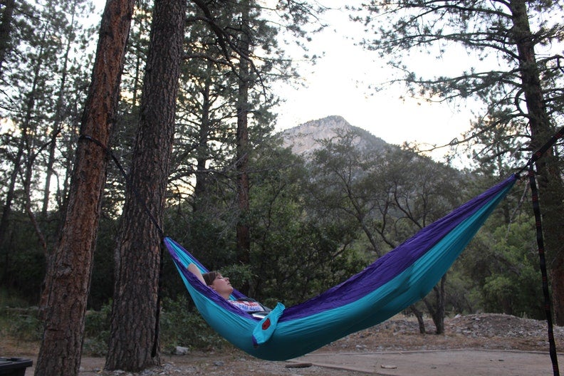 Women relaxing in blue hammock within the forest.