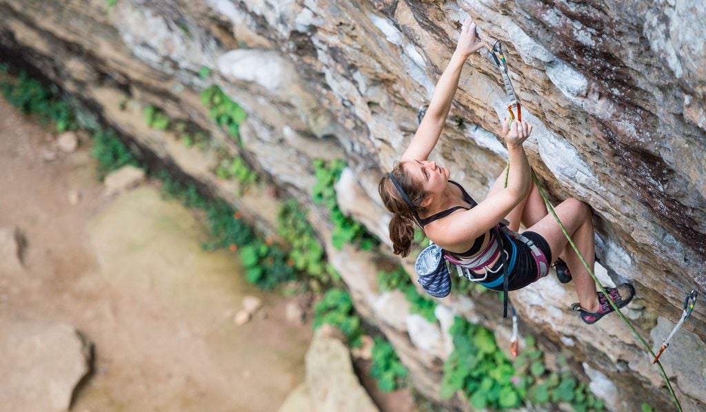 climber makes her way up an outdoor rock wall in the daytime