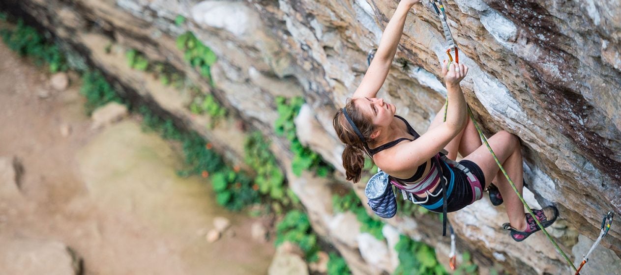 climber makes her way up an outdoor rock wall in the daytime