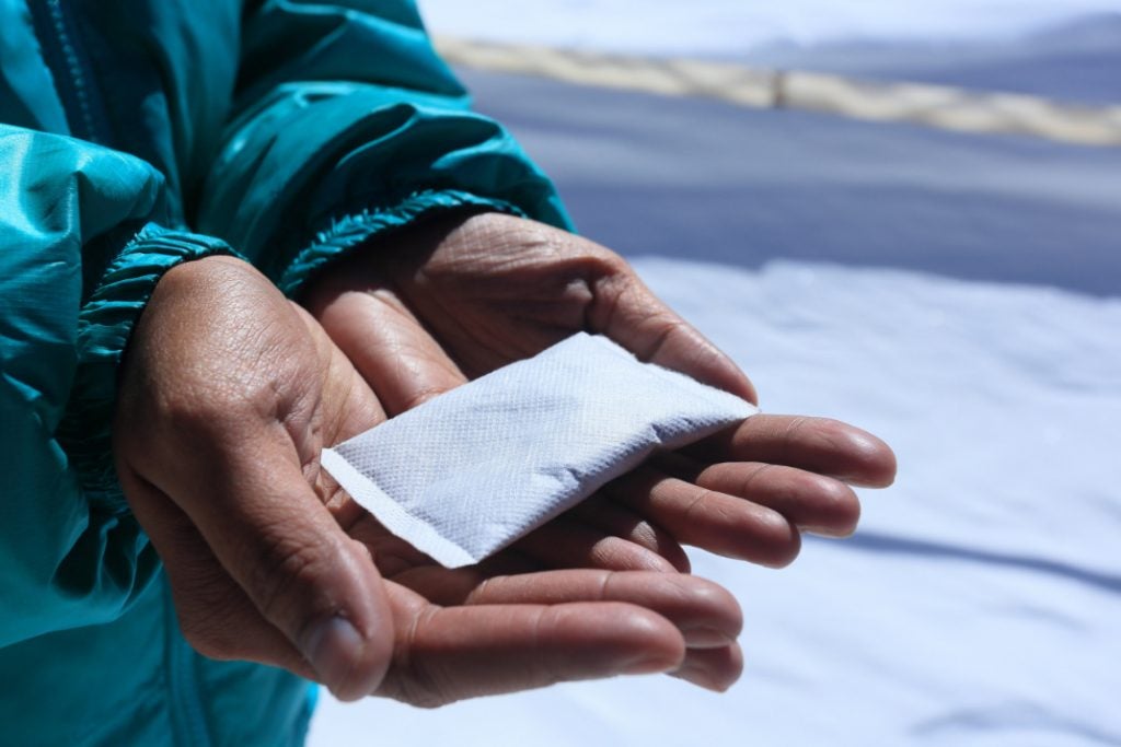 hiker in teal jacket holds hand warmer in two hands with snow in the background