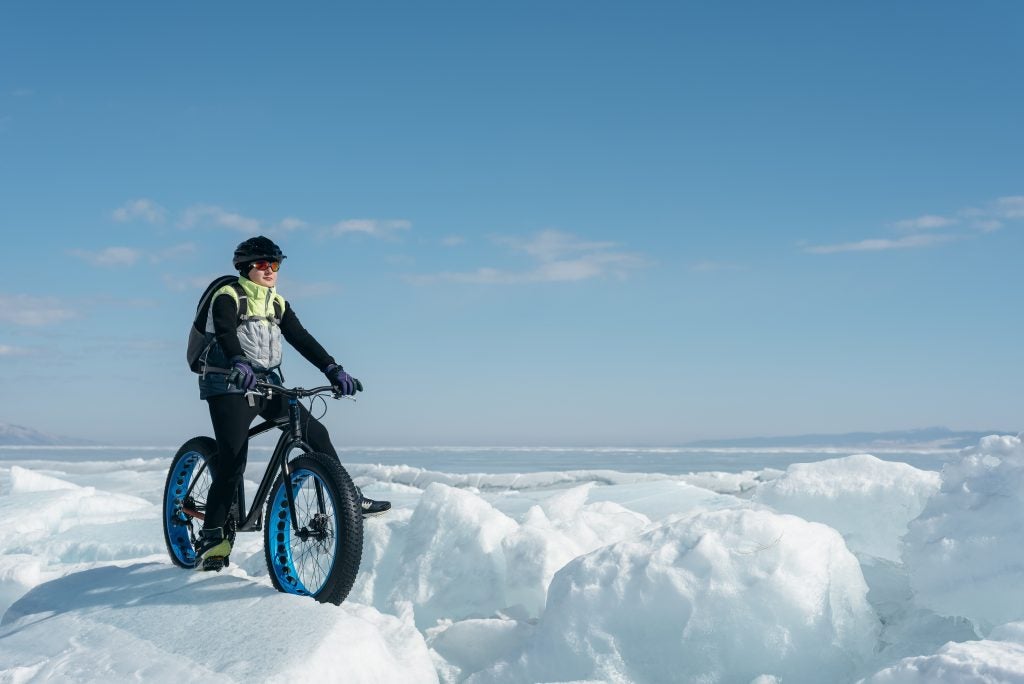 cyclist on a fat tire bike traverses large snow mounds on a clear winter day