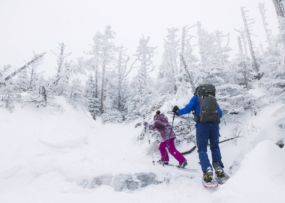 A man and a young girl snowshoeing up a snowy mountain