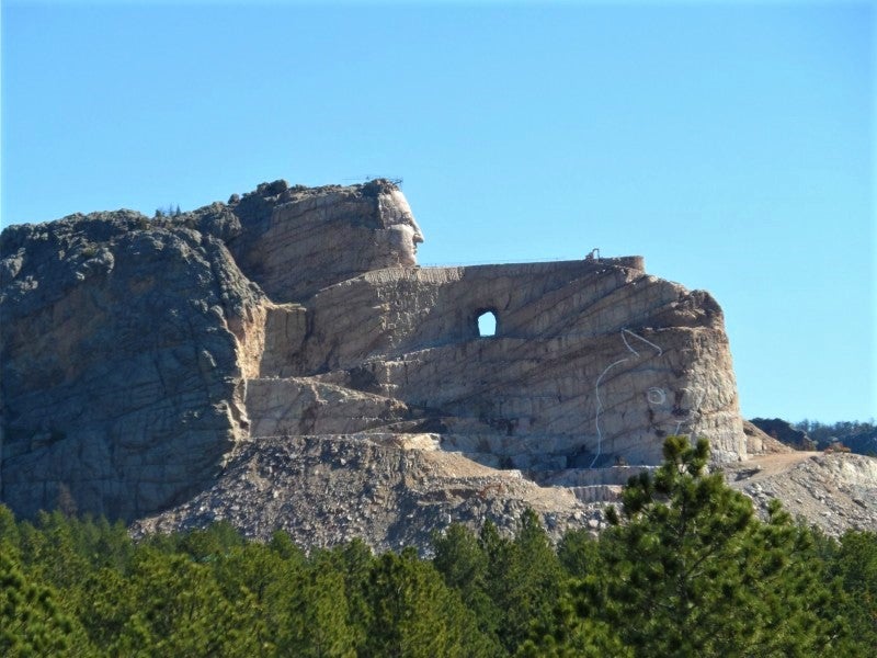 looking over trees towards the construction of the Crazy Horse Memorial