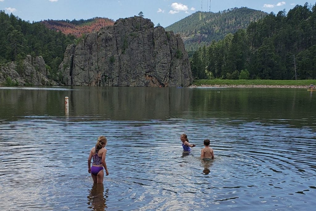 children swim in legion lake near large rock wall