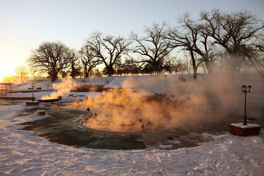 a snowy winter scene at sunset in Utah while people soak in steaming hot springs on the ground