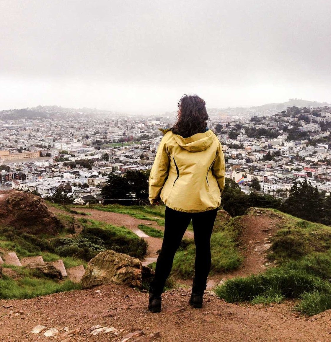 hiker in a yellow jacket overlooks san francisco bay area on a foggy day