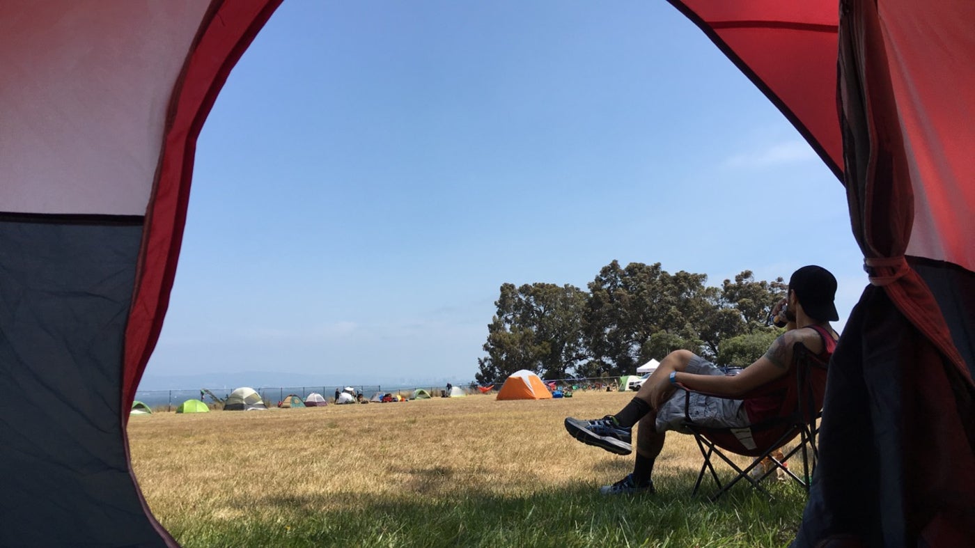 man in camp chair overlooking group tent site is visible from inside red tent