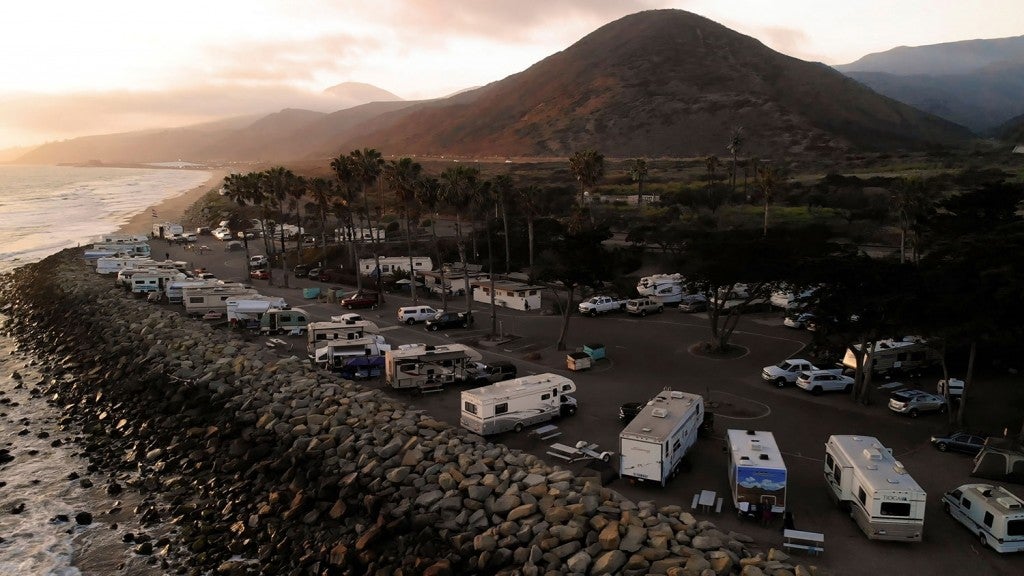 RVs in line in front of a mountain near a coast while beach camping in california