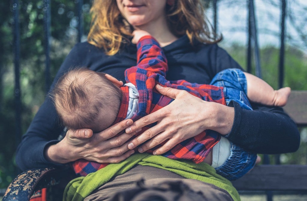 a woman holding a newborn baby and breastfeeding them in the outdoors