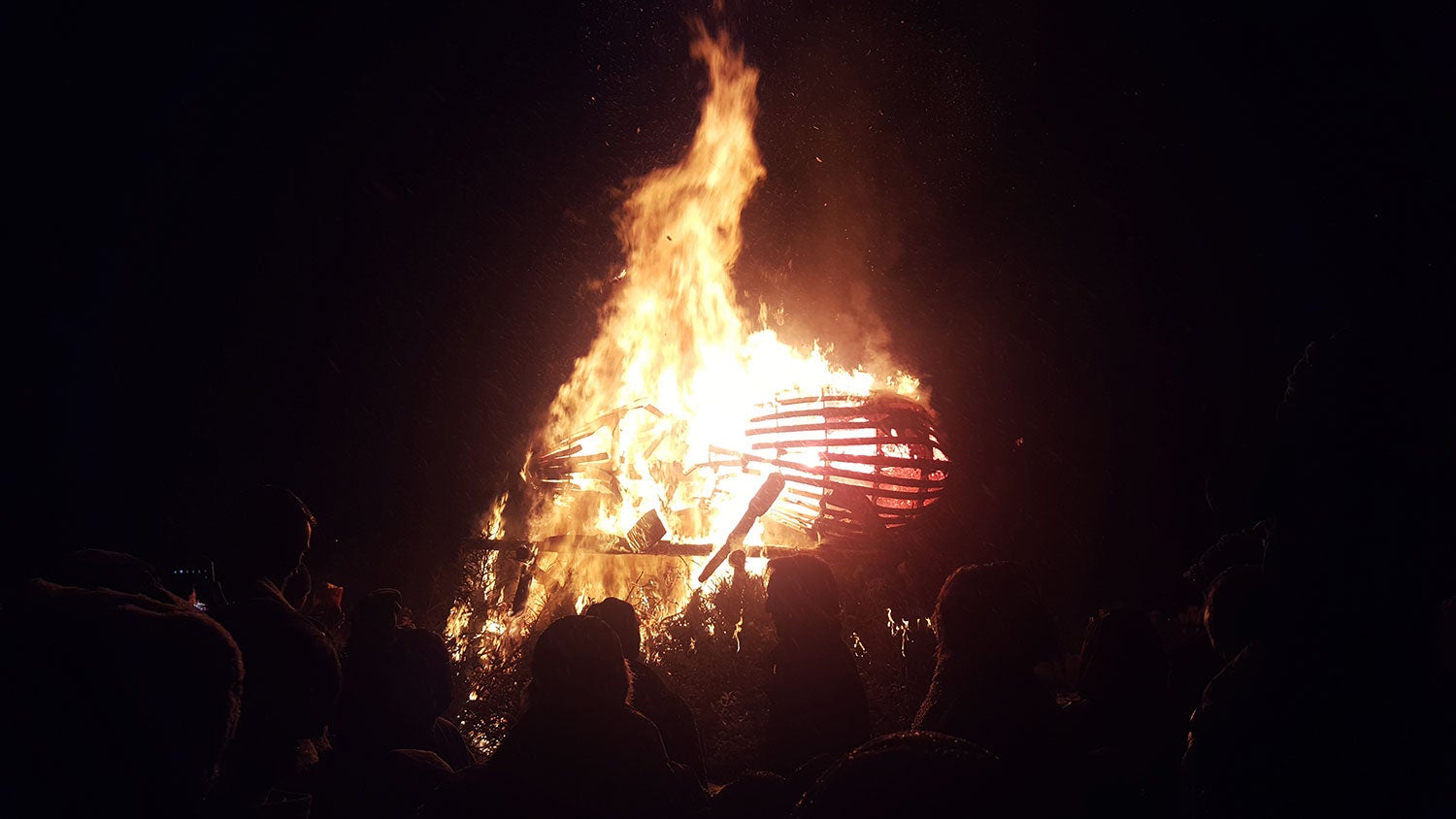 a wooden beetle burning at night around a crowd