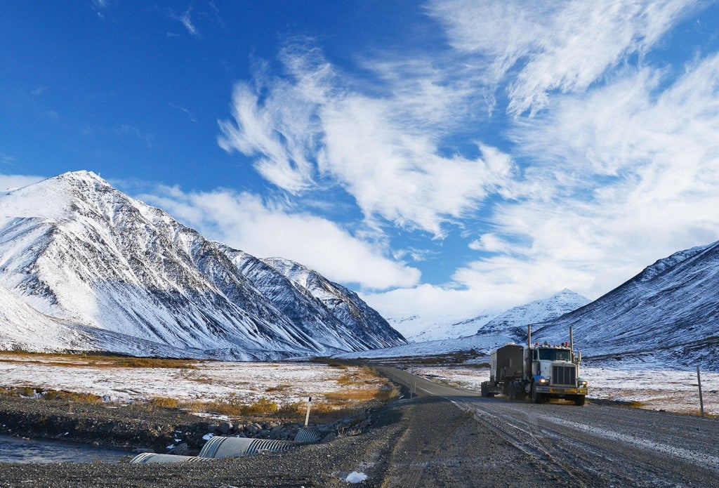 freight truck drives up a snowy dalton highway with mountains visible in the distance