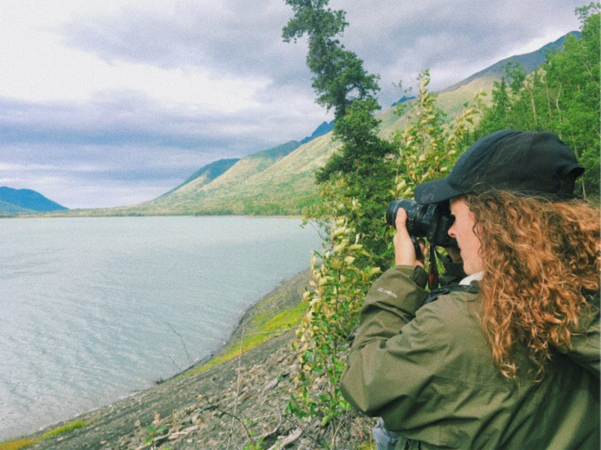 Woman with brown curly hair in a green raincoat photographing waterway near chugach state park