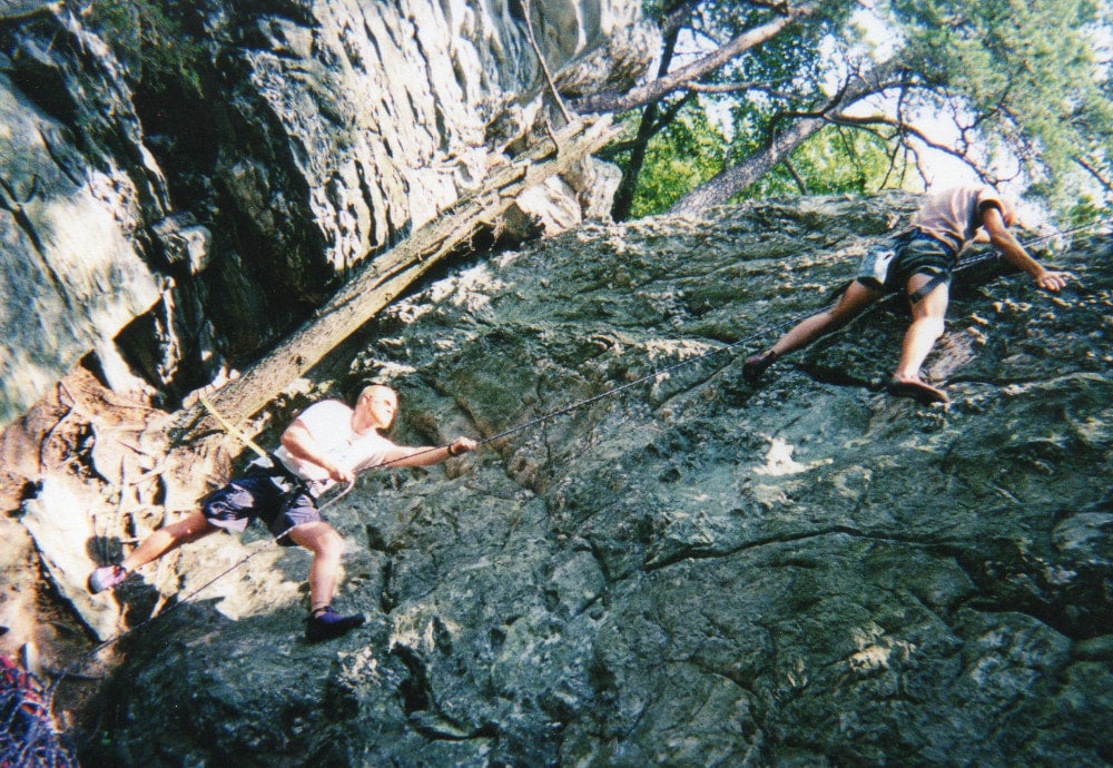 Two men climbing a rock wall, one man belaying the other in the summertime at North Carolina's Pilot Mountain State Park