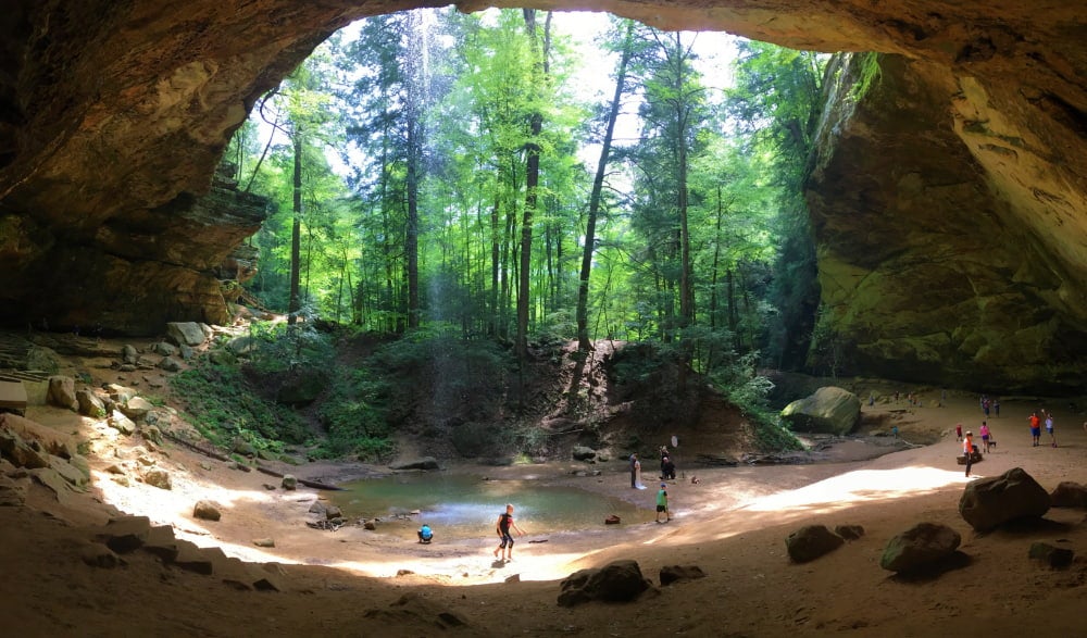 visitors scattered around waterfall visible from inside a large cave in hocking hills state park