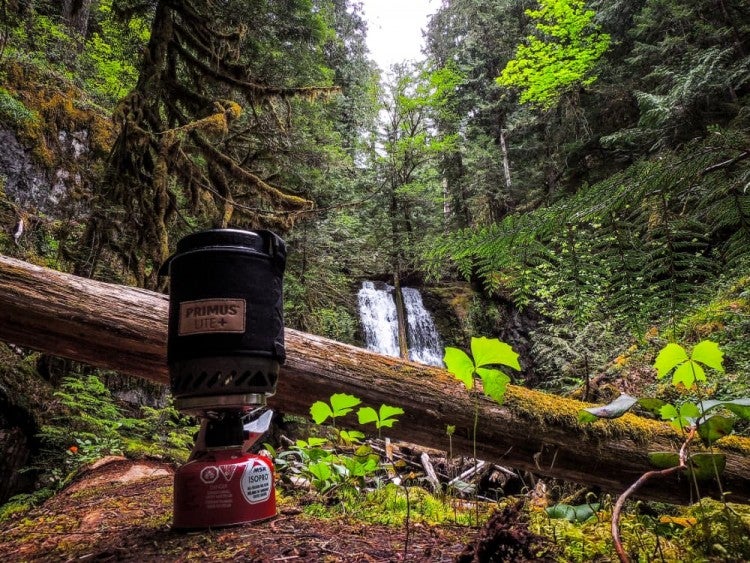 small primus backpacking stove in front of waterfall in mossy forest