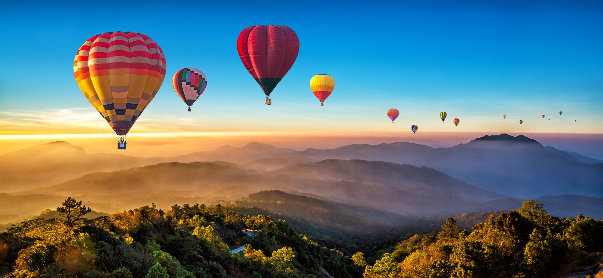 multiple hot air ballons floating above mountains at dawn