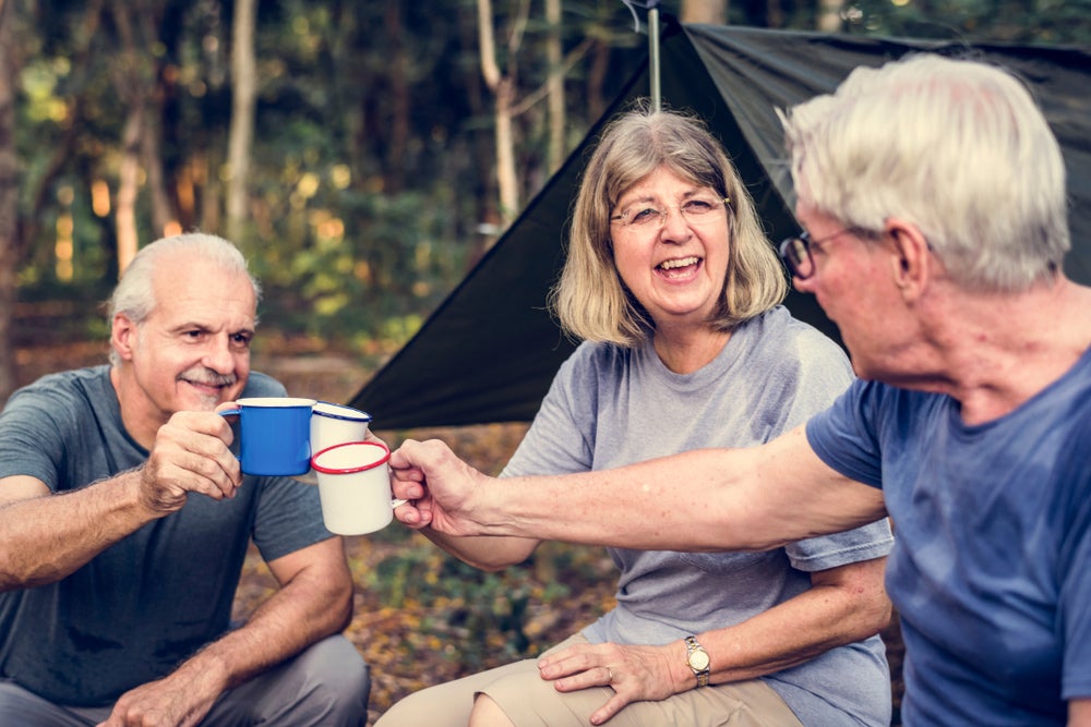 three seniors gathered in wooded campsite toasting with their mugs