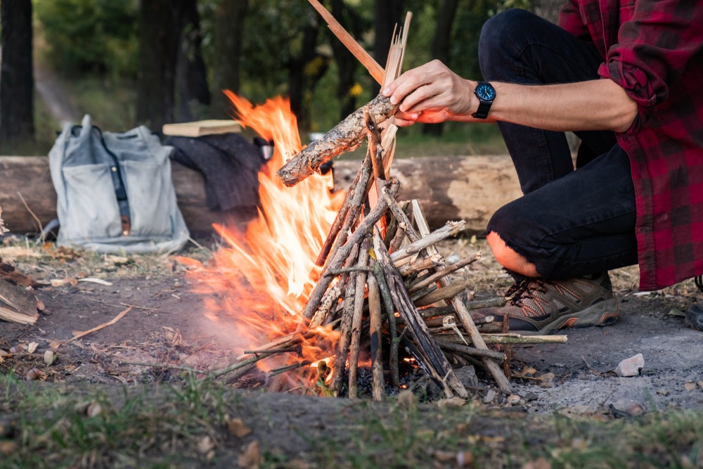 man places stick atop freshly constructed teepee campfire