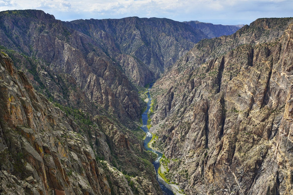 panoramic of steep rugged rocks that lead to small river in black canyon of the gunnison