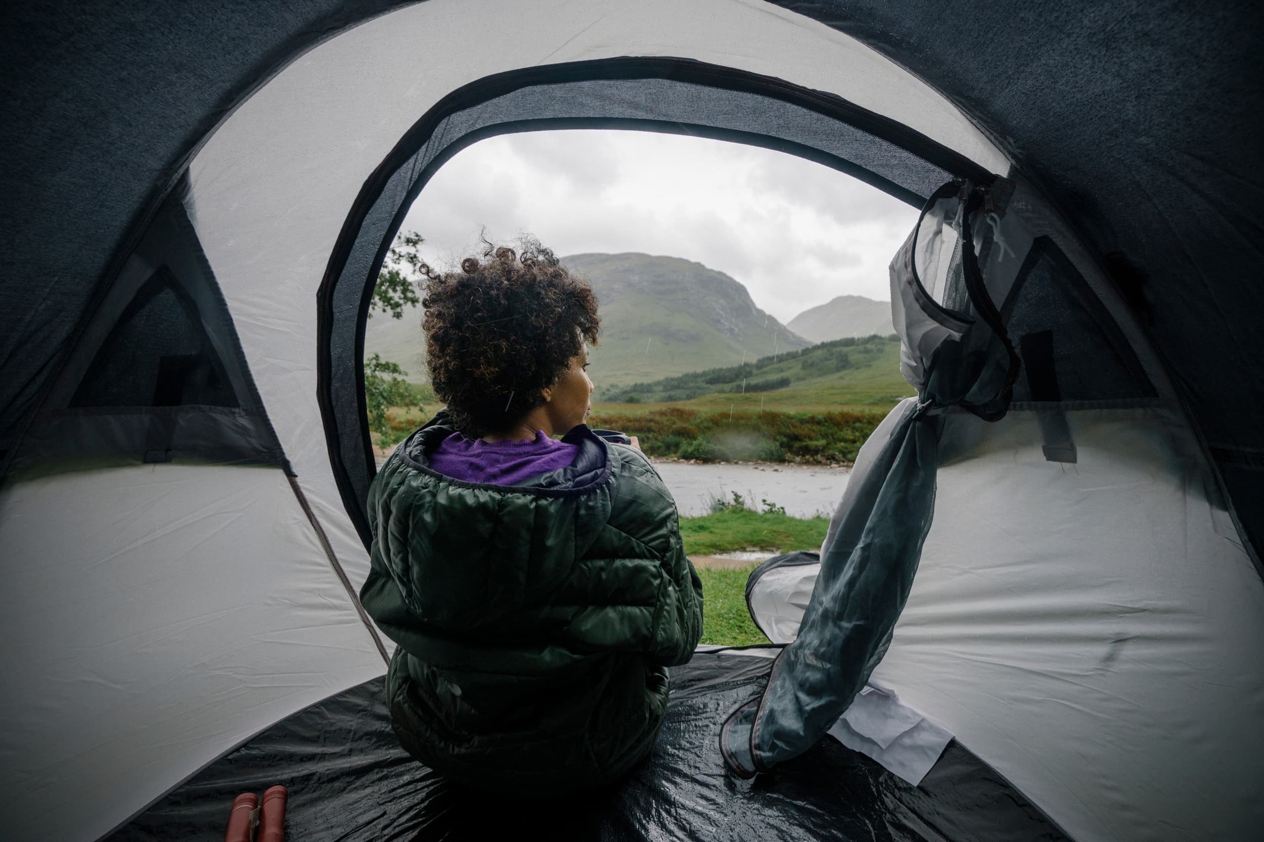 woman attempting to stay dry while gazing out at rainy hillside from inside waterproofed tent