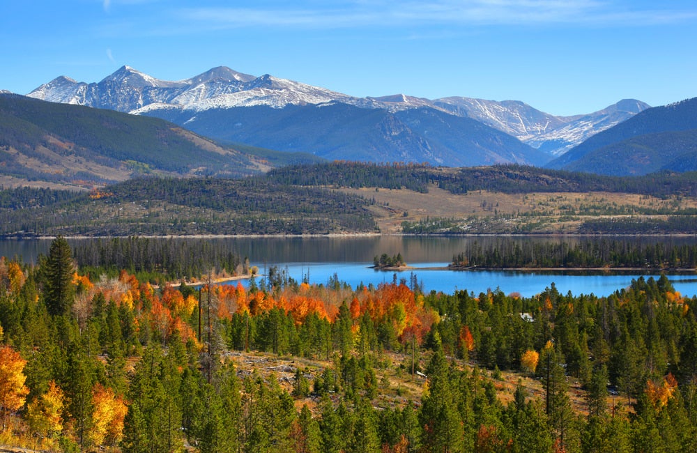 large mountains visible in the distance from alpine lake surrounded by fall foliage